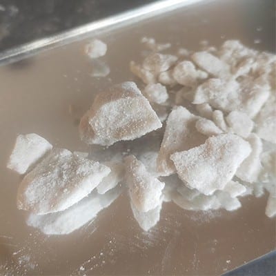 Buy KU Crystals Online: High-Purity KU Crystals for Research and Chemical Studies 1 Close-up of high-purity KU crystals scattered on a reflective surface, showcasing their crystalline structure and white color, suitable for research and chemical studies.