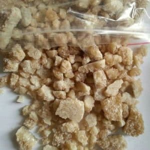 Close-up of light brown MDMA crystals spilling out of a clear plastic bag onto a white surface.