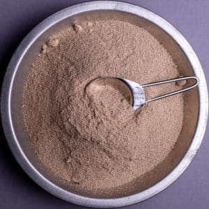 A close-up view of a silver tray filled with a fine, light brown powder, with a measuring scoop partially embedded in the powder. The image represents MDPHP, a chemical used for neurochemical research and studies.