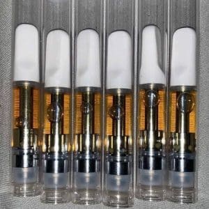Six clear vape cartridges filled with amber liquid, each featuring a white mouthpiece and a metallic base, arranged in a row.