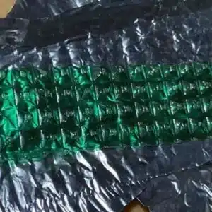 Close-up of a row of green gelatin tabs, arranged in a diamond pattern, resting on crinkled black packaging.