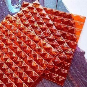 Three sheets of orange, pyramid-shaped LSD blotter paper arranged on a dark surface, showcasing a high-quality design.