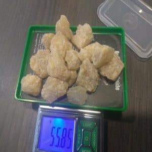 A digital scale displaying 55.85 grams, with a green tray holding several yellowish MDMA crystal chunks on a wooden surface.
